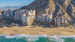 A coastal hotel complex with multiple buildings, a beach, and a rocky cliff. - Oceanfront resort, semi-private beach within walking distance to all amenities (Cabo San Lucas)