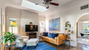 A living room with a sofa, ottoman, TV, and a large painting. - 2 Mi to Downtown: Pet-Friendly Home in Phoenix! (Phoenix)