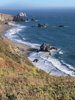 A coastal landscape with rocky outcrops and waves crashing onto a sandy beach.