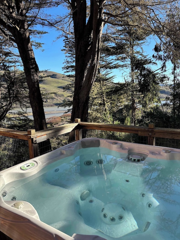 A hot tub surrounded by trees with a view of a lake and hills in the background.