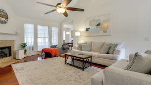 A spacious living room with a fireplace, a ceiling fan, and a large abstract painting. - 11 Mi to Savannah! Suburban Home w/ Spacious Yard (Pooler)