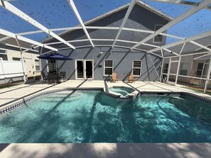 A swimming pool with a tiled edge, surrounded by a covered patio area with chairs and an umbrella. - Bloomingdale Oasis with EV Charger (Davenport)