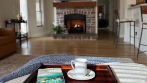 Uma sala de estar acolhedora com lareira, um tabuleiro com xícara e livro, e um quadro grande acima da lareira.
