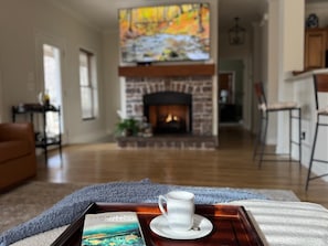 A cozy living room with a fireplace, a coffee tray with a cup and a book, and a large painting above the fireplace.