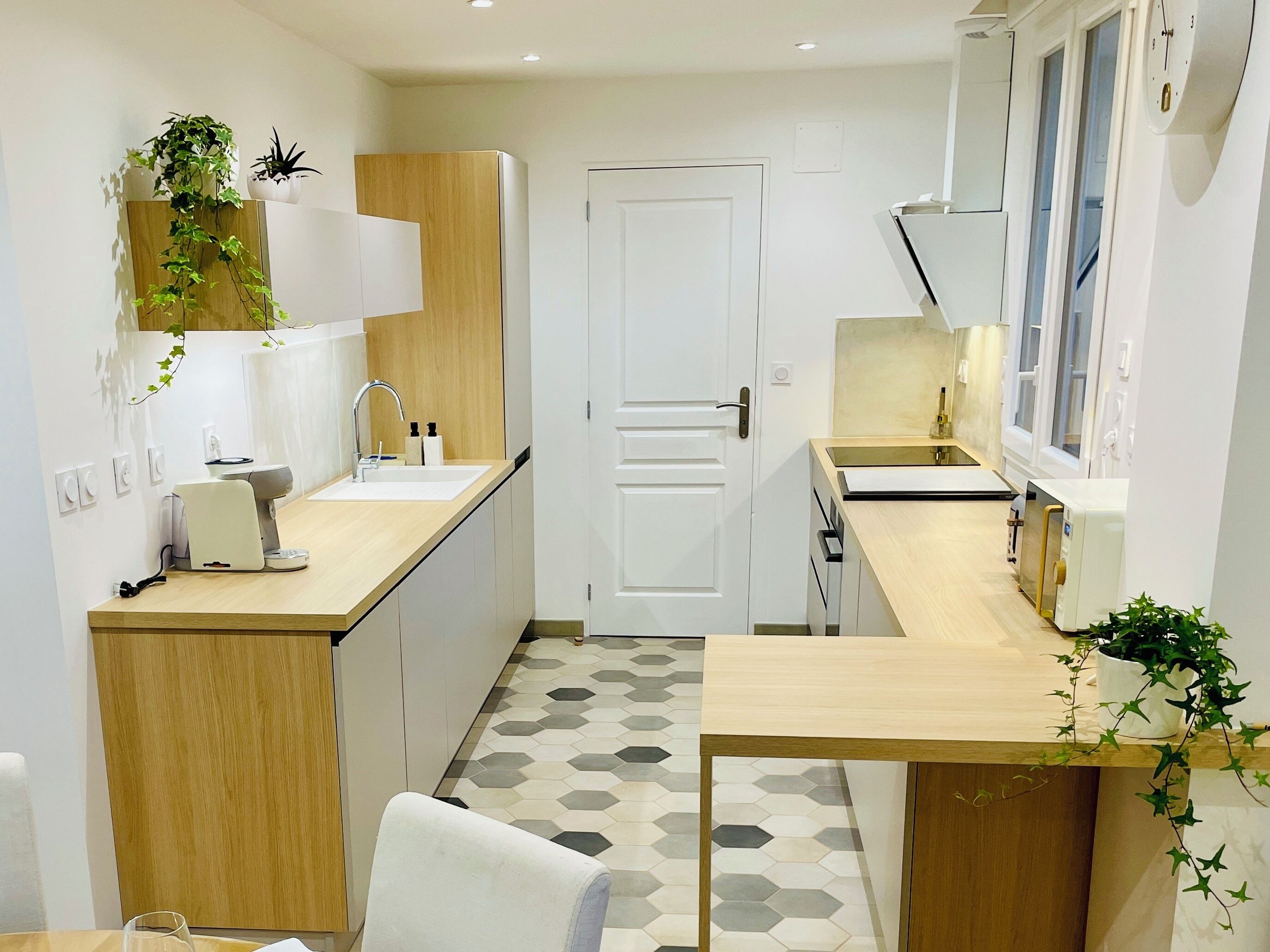 A modern kitchen with a wooden countertop, a sink, and a door. There are plants on the wall and a clock on the wall.