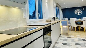 Une cuisine moderne équipée d’un lave-vaisselle, un coin repas avec une table et des chaises, et un mur décoré d’un motif représentant un arbre.