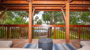 A covered outdoor area with wooden beams, a pool, and a view of a landscaped garden. - Waterfront 6BR Oasis • Pool • Gym • Huge Dock (Riverview)