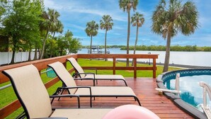 A wooden deck with lounge chairs, a pool, and a view of a lake with palm trees. - Waterfront 3BR Villa w/ Gym/Pool & Dock Access (Riverview)