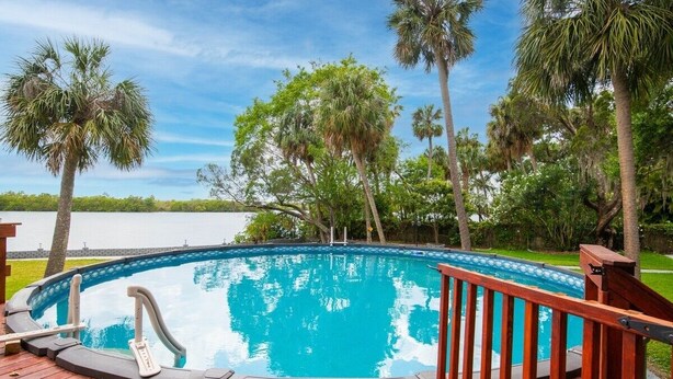 A swimming pool with a wooden deck, surrounded by palm trees and a view of a body of water. - Waterfront 3BR Villa w/ Gym/Pool & Dock Access (Riverview)