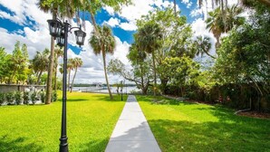 A pathway lined with trees and a lamp post, leading towards a body of water with a bridge in the background. - Waterfront 3BR Villa w/ Gym/Pool & Dock Access (Riverview)