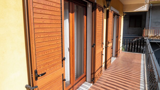 Eine Holztür mit Glasfenster, einem Metallgriff und einer kleinen Stufe, die zu einem Balkon führt.