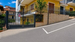 Ein begrenzter Eingang mit einem 'Verboten zu parken'-Schild, eine Steinmauer und ein gelbes Gebäude mit einem Balkon.