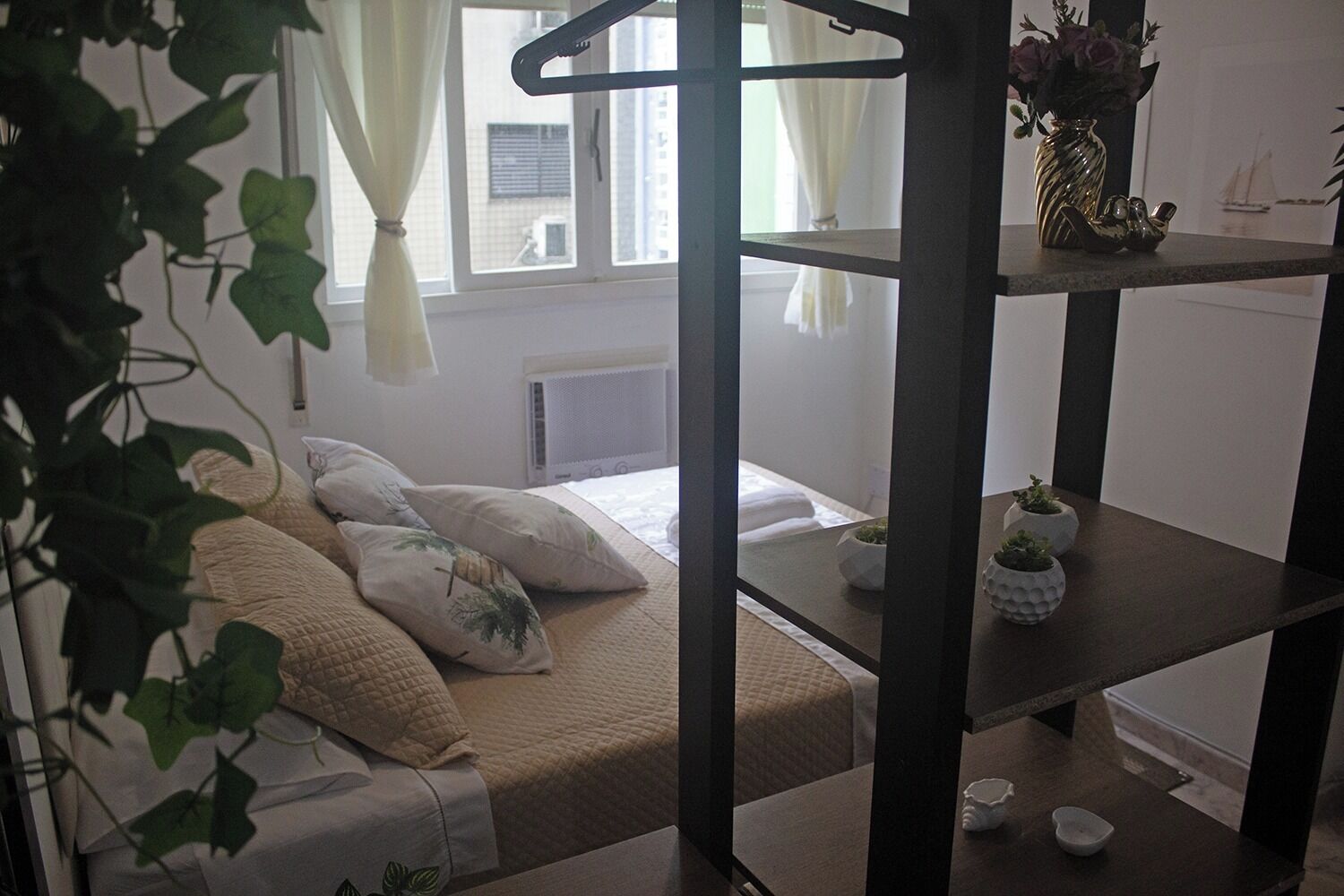 Een kleine kamer met een stapelbed, een klein tafeltje met planten, en een raam met gordijnen.