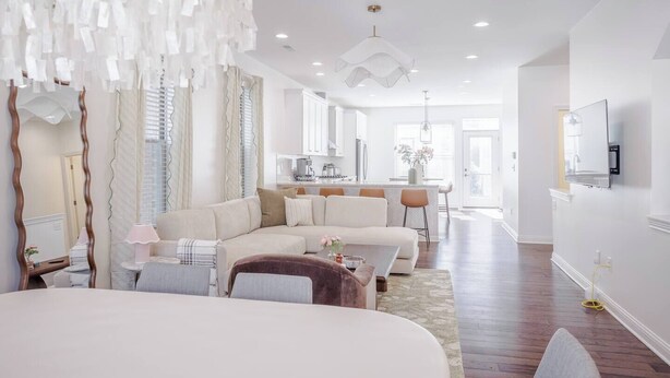 Un salon moderne et bien éclairé, avec un grand canapé, un coin repas et une cuisine en arrière-plan.