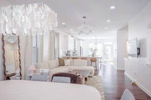 Un salon moderne et bien éclairé, avec un grand canapé, un coin repas et une cuisine en arrière-plan.