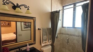 Een badkamer met een wastafel, toilet, douche, spiegel en een raam.