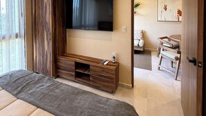 A bedroom with a large bed, a TV mounted on the wall, wooden furniture, and a view of the bathroom. - 10 min. from beach, New luxury condo w/ Pool, Gym, Sauna, Parking and laundry! (Playa del Carmen)