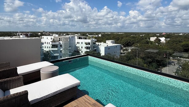 A rooftop infinity pool with white lounge chairs and a view of surrounding buildings. - 10 min. from beach, New luxury condo w/ Pool, Gym, Sauna, Parking and laundry! (Playa del Carmen)