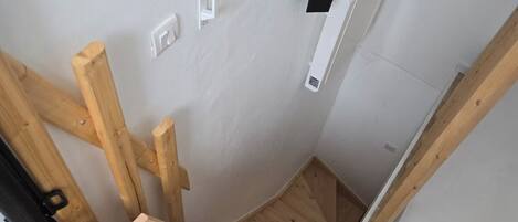 A narrow, wooden staircase with a handrail, white walls, and a small black shelf.