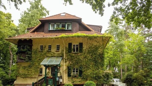 A two-story house with a sloped roof, ivy-covered walls, and a gravel driveway. - Strandvilla Hubertus - H1 - Marc Chagall (Ostseebad Boltenhagen)