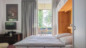 A bedroom with a wooden bed, a television on a dresser, and a view of the outdoors. - Strandvilla Hubertus - H1 - Marc Chagall (Ostseebad Boltenhagen)