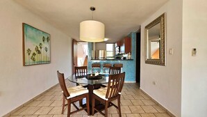 A dining area with a round table and chairs, a large pendant light, and a kitchen in the background. - Oceanfront Escape 3BR 2BA Pool Parking Private Beach Access Loíza (Loíza)
