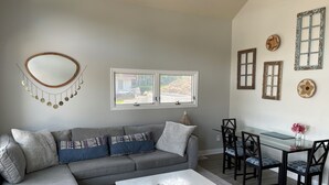 A modern living room with a grey sectional sofa, a white coffee table, and a dining area with black chairs and a glass table.