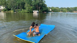 A couple on a blue floating platform in a calm lake surrounded by trees and houses.