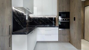 A modern kitchen with white cabinets, black marble countertops, and stainless steel appliances. - Plaza Luxury Suite | 2’ from Metro | 5’ from Piraeus (Koridallos)