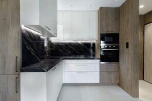 Una cocina moderna con armarios blancos, encimeras de mármol negro y electrodomésticos de acero inoxidable.