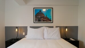 A hotel room with a large bed, two bedside tables with lamps, and a framed picture of a building on the wall. - w* | Chic & Inviting 2BR w/ Balcony in Miraflores (Miraflores)