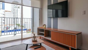 A modern living room with a large TV, a wooden cabinet, and a small table with a remote control. - w* | Chic & Inviting 2BR w/ Balcony in Miraflores (Miraflores)