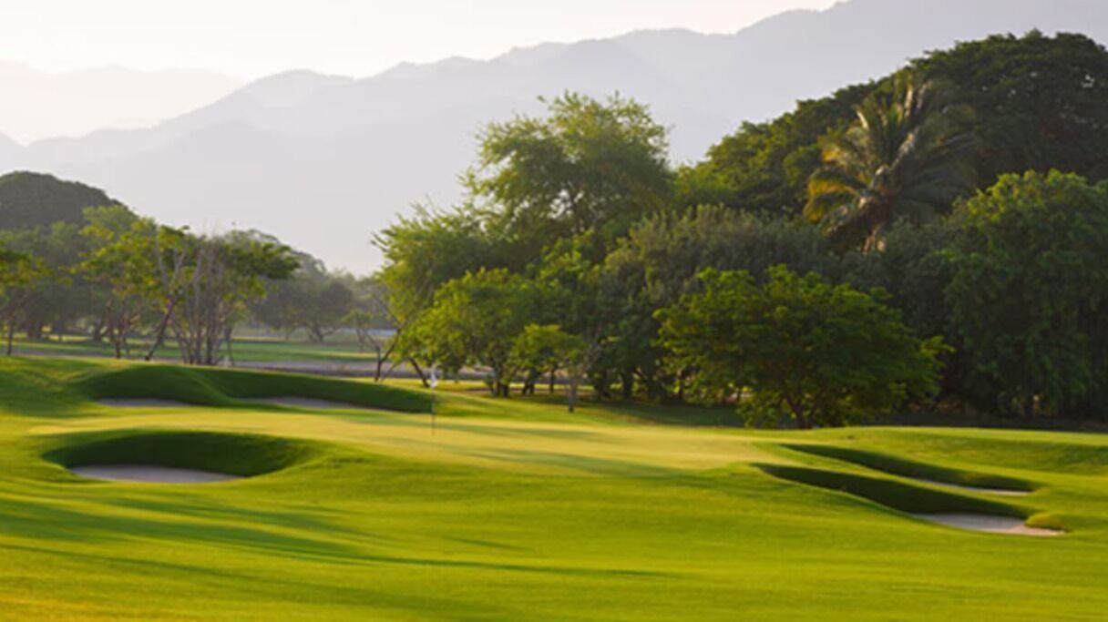 A golf course with sand bunkers, trees, and a mountain backdrop.