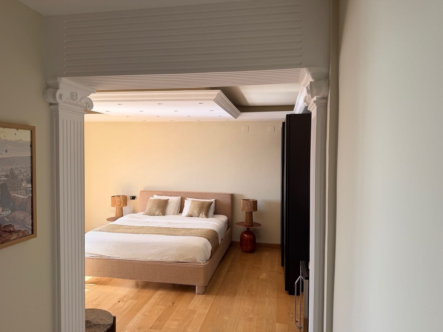 Quarto com cama, luminárias de cabeceira e vista através de uma porta aberta.