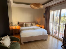 Un dormitorio con una cama grande, lámparas de noche, una silla y vistas a través de una ventana.