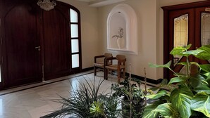 Un'ampia hall con un'imponente porta in legno, un lampadario, una zona salotto con poltrone e una pianta in vaso.