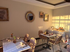 Un comedor con sillas y mesas de mimbre, un espejo redondo con marco dorado y obras de arte enmarcadas en la pared.