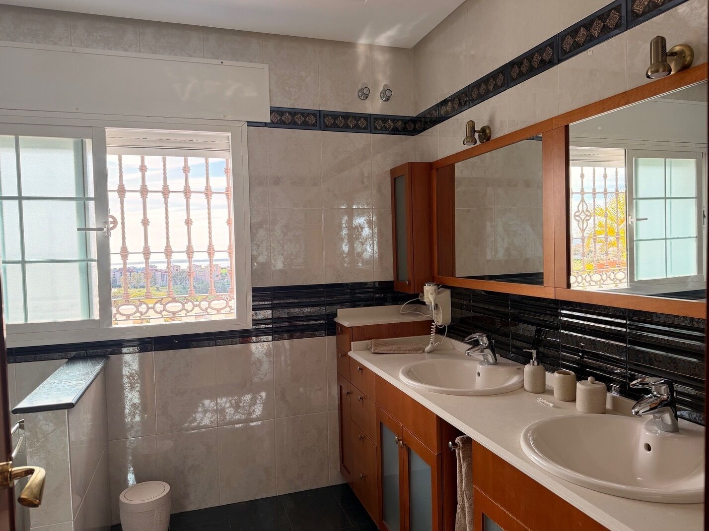 A modern bathroom with two sinks, a large mirror, and a window with a view of buildings.