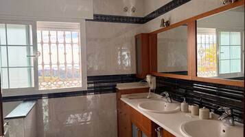 A modern bathroom with two sinks, a large mirror, and a window with a view of buildings.