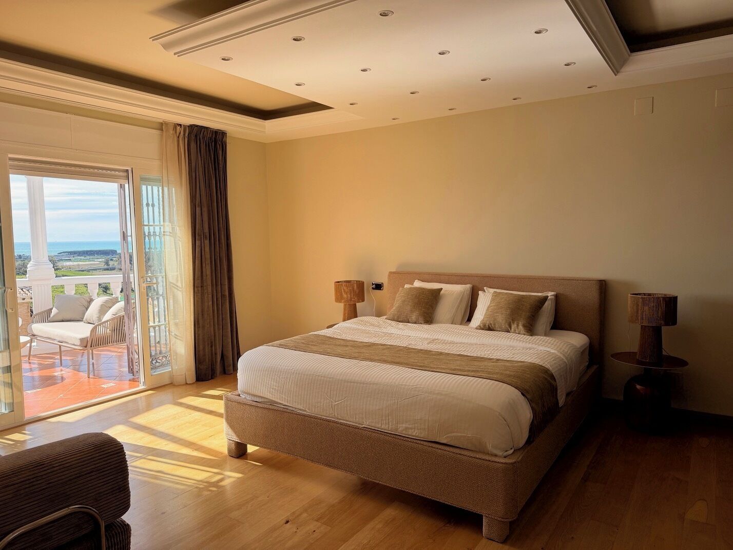 A spacious bedroom with a large bed, two bedside lamps, and a view of the outdoors through a sliding glass door.