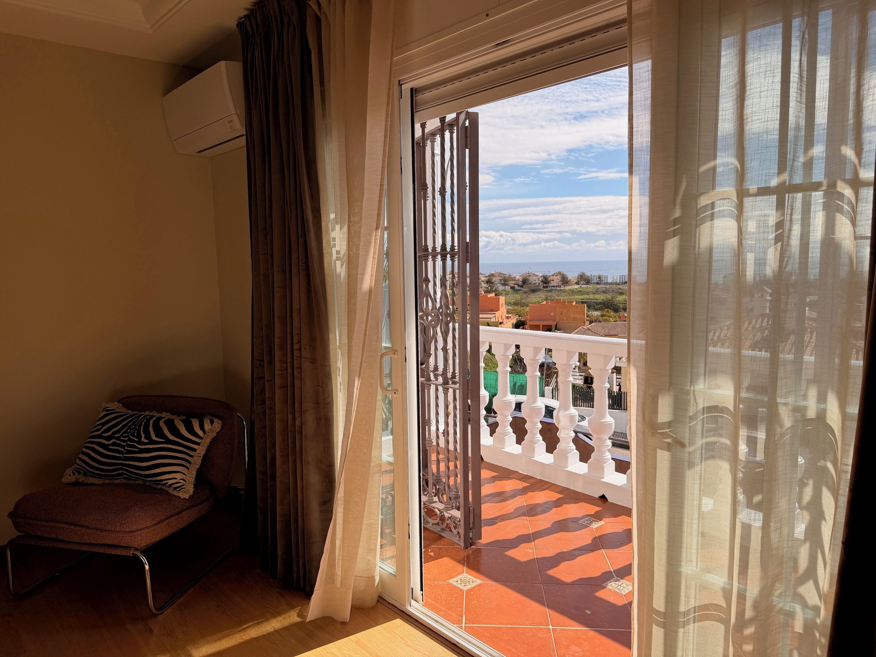 Un balcón con vista a un paisaje lejano, una silla con un cojín de estampado de cebra y una puerta corrediza de vidrio.