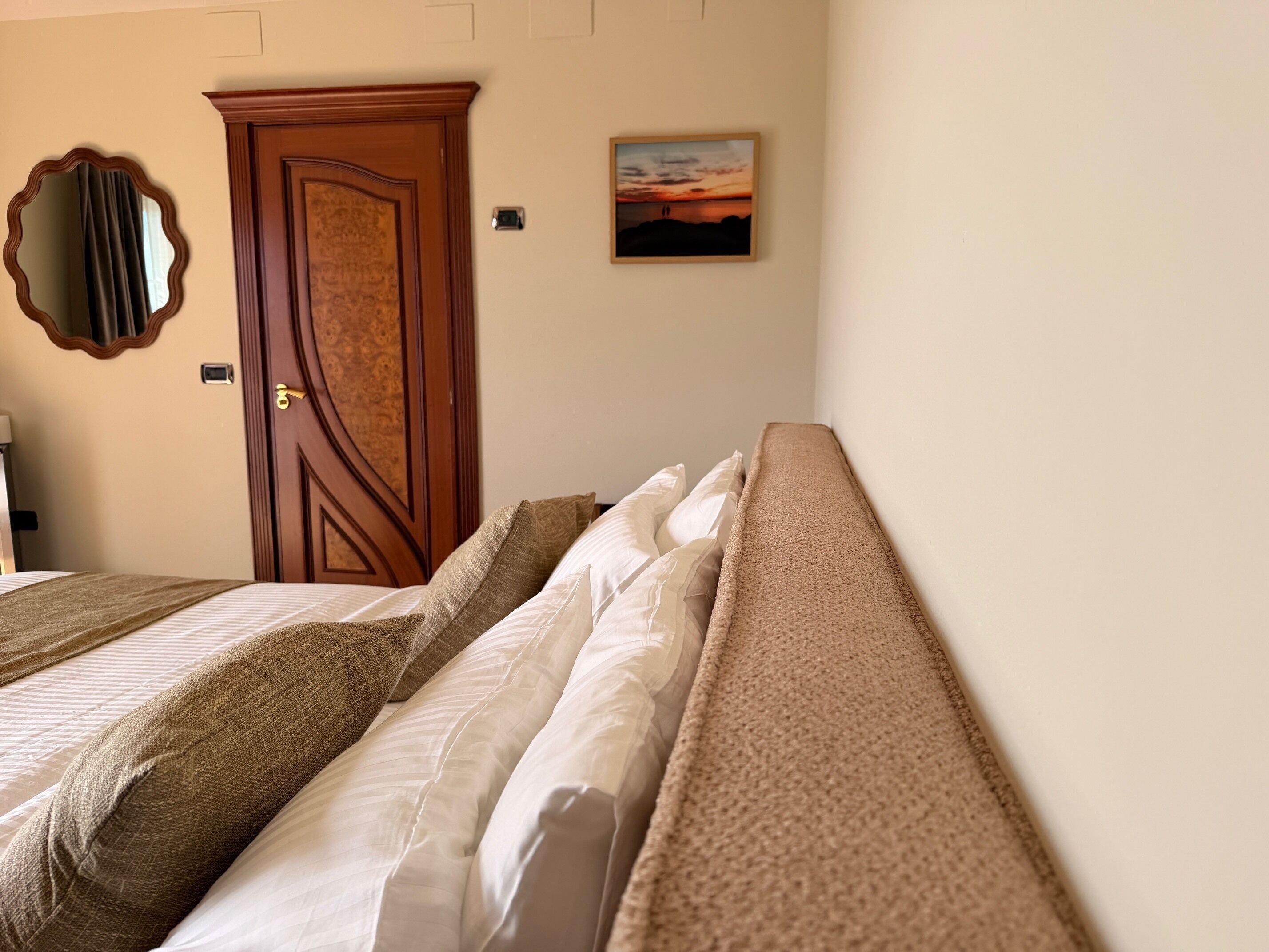 A hotel room with two beds, a wooden door, a mirror, and a painting on the wall.