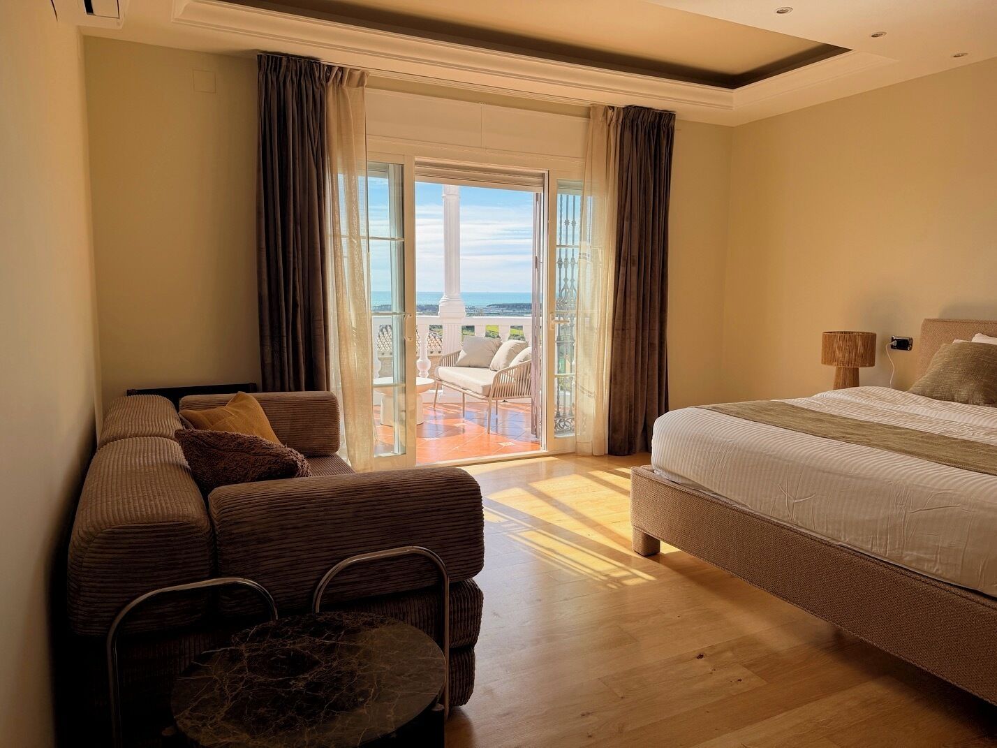 Habitació d'hotel amb llit, sofà, taula petita i balcó amb vistes.
