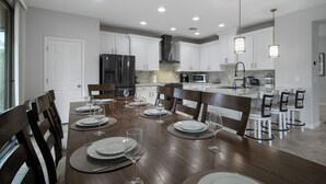 Una cocina moderna con armarios blancos, una isla central y un comedor preparado para seis personas.