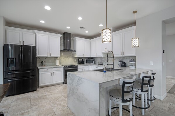 A modern kitchen with white cabinets, stainless steel appliances, a marble island, and bar stools. - Westgate Retreat, Family & Pet-Friendly 4BR Home (Glendale)