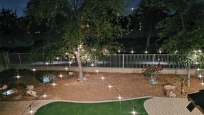 Un jardín ajardinado con césped bien cuidado, iluminación decorativa y una valla blanca.
