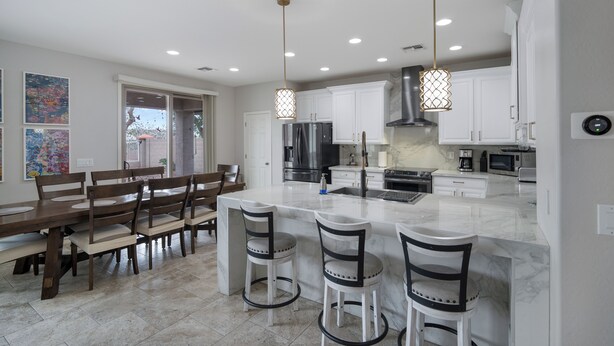 Una cocina moderna con armarios blancos, una isla grande con taburetes de bar e iluminación colgante.