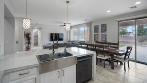 Una cocina moderna con una isla central, comedor con banco y un amplio ventanal corredera que da a un patio.