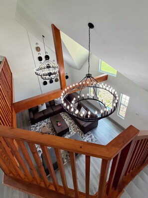 Ein Loft-Zimmer mit einer Holztreppe, einer Chandelier, einer Sofagarnitur und Blick ins Freie.