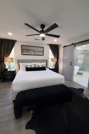 Ein modernes Schlafzimmer mit einem großen Bett, einem Deckenventilator und einer Schiebetür zu einem Badezimmer.
